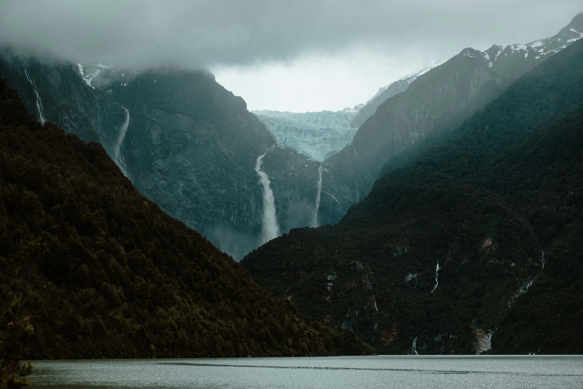 Glaciar colgante y cascada entre montañas cubiertas de nubes en Aysén